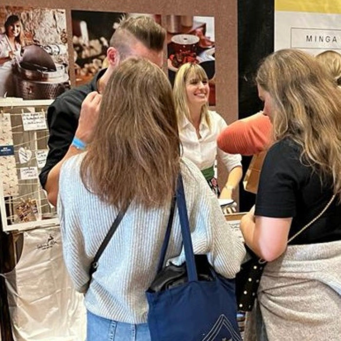 Zwei Besucherinnen stehen vor dem Messestand der „Sabrina Alm Genussmanufaktur“, betrachten Produkte und sprechen mit einer Frau hinter dem Stand.